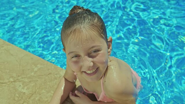 A little girl is having fun in the pool.Little girl in pink swimsuit swimming in pool and smiling at camera