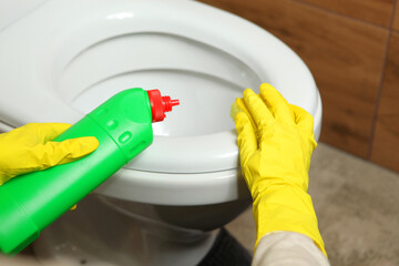 Woman washing and disinfecting toilet bowl with detergent close-up