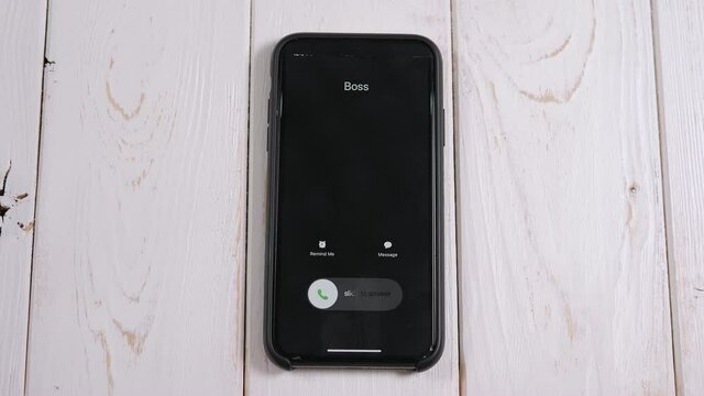 A close-up of an incoming call from the boss on a mobile phone screen on a light wooden background.