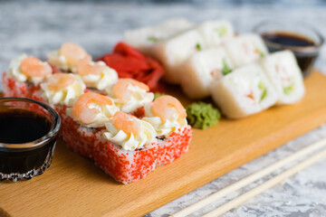 Delicious sushi rolls with chicken, cheese, shrimp, red ginger, wasabi and soy sauce on a wooden board on a light background with copy space