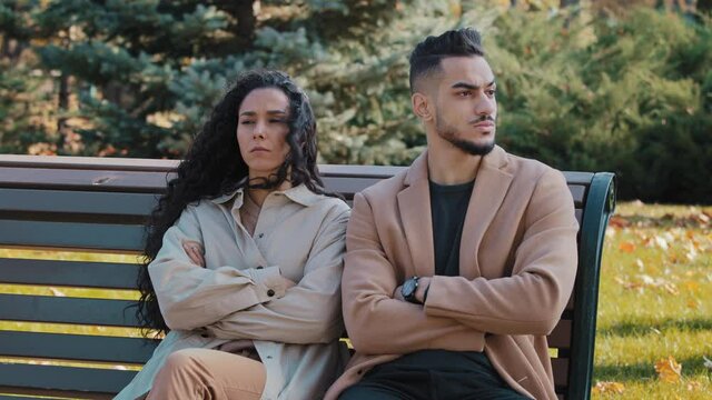 Sullen couple sitting on bench in park man and woman sit with arms crossed lovers quarrel ignoring each other angry arabic guy and curly offended girl feel sad sadness from conflict misunderstanding