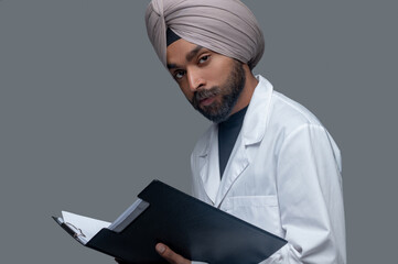 Calm Indian doctor in the turban holding medical documents