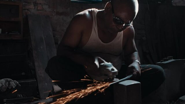 Blacksmith polishing knife blade using grinder, sparks flying