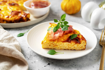A piece of frittata with pumpkin, bacon and ricotta in a ceramic plate on a light culinary background. Traditional Italian delicious homemade egg dish on the kitchen table closeup	