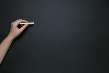 hand with chalk on black chalkboard, place for text, basis for design, left-handed concept