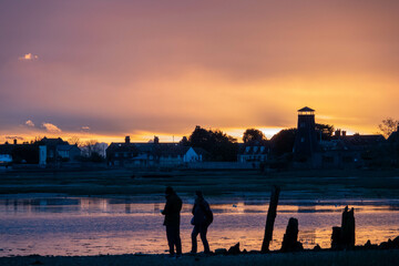 people silhouetted on the beach at sunset with Langstone Harbour and Mill Hampshire England in the background