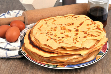 Crêpes empilées dans une assiette à côté d'ingrédients et d'ustensiles de cuisine