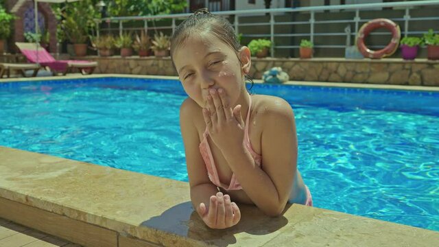 Happy girl sending a kiss to the camera.A little girl is having fun in the pool. Little girl wearing color swimsuit swimming in pool and smiling at camera.