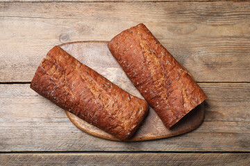 Cut rye baguette on wooden table, top view