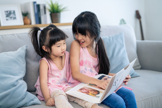 Asian big sister showing old album recalls the past to younger sibling