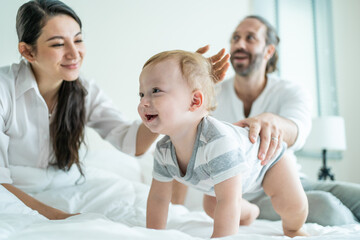 Caucasian parents playing with cute baby boy child on bed in bedroom.