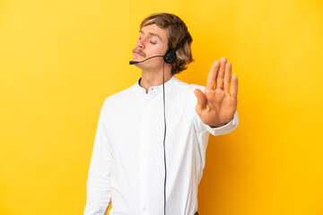 Telemarketer man working with a headset isolated on yellow background making stop gesture and disappointed