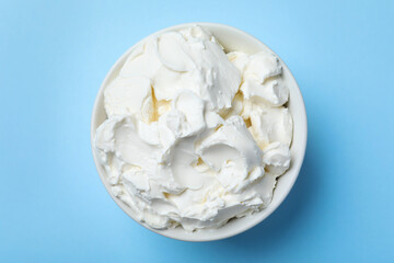 Bowl of tasty cream cheese on light blue background, top view