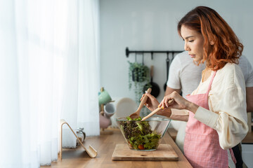 Asian beautiful woman cook green salad with husband in kitchen at home