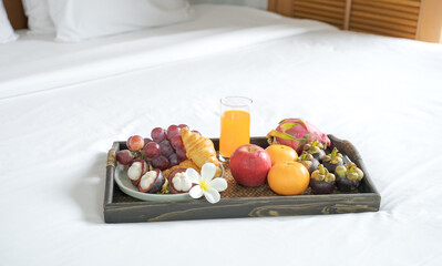 Breakfast, fruit, croissants, orange juice, in a black wooden tray, on a white bedsheet, Healthy food concept