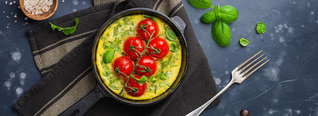 Frittata with arugula, potatoes and cherry tomatoes in iron pan on old stone table background. Top view.