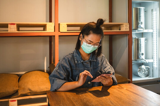 Asian businesswoman slides her phone to check products in front of the beer keg freezer. Small business concept