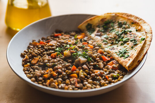 lentils homemade vegan dish with vegetables and carrots and smoke, with an indian roti bread on the side with parsley leaves. soft natural light