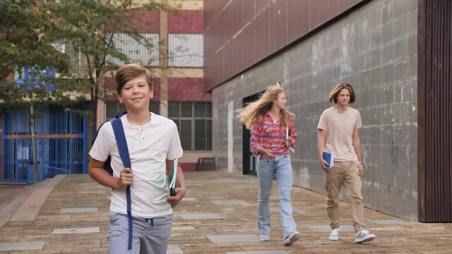 Teenager boy going home after classes in school with other teens who walking in background. 