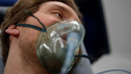 Injured man in oxygen mask lying on stretchers in ambulance car