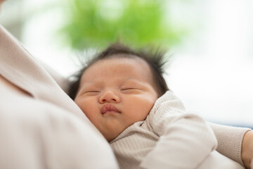 Adorable sleeping newborn baby relax in mother arm safety and comfortable.Smile Asian newborn infant baby resting sleeping sweet dream.Mother holding infant baby.Newborn Baby photography concept