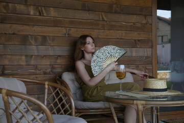 Young woman enjoying a glass of wine on the cozy wooden balcony during summer afternoon