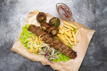 fried beef lula kebab with fried potatoes and mushrooms on the parchment paper and wooden.