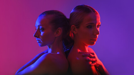 two beautiful adult girls are touching with their backs - neon light