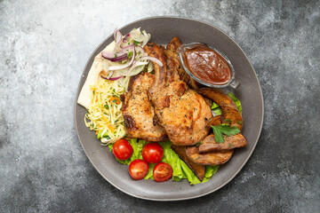 Grilled pork (neck) with tomatoes and green letuce salad, cabbage salad and red onion on the plate. top view. Grey background.