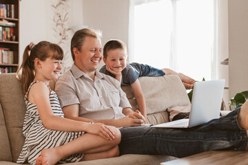 Fototapeta na wymiar Video conference. Dad and the children are sitting in the living room and are making video calls to mom and grandmother and smiling. Communication, meetings online