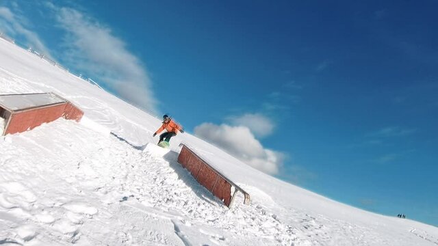 Snowboarder with shining orange suit filmed by fpv drone while doing tricks on the rail bank 60fps