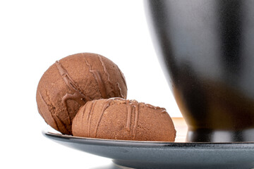 Two sweet chocolate cookies on a ceramic saucer with a cup, close-up, isolated on white.