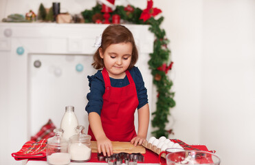 Little cute girl in red apron baking Christmas cookies at home