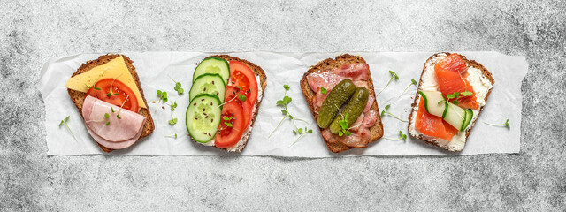 Set of different open sandwiches with meat, vegetables and fish on gray grunge background. Various...