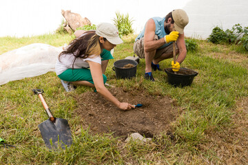 Pareja hombre y mujer latinos preparando el suelo en el jardín verde para construir un fogón con piedras naturales. Concepto de bioconstrucción ecológica, herramientas de jardinería, trabajo en equipo
