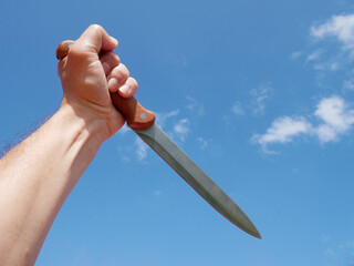 Fist holding a large knife on blue sky background