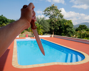 Hand holding a large knife on swimming pool background, murder concept