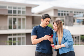 Hermosa pareja multiétnica conversando y utilizando tecnología muy feliz en exterior	