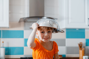 Happy daughter portrait playing in kitchen. Child kid girl Soiled in flour put colander bowl on...