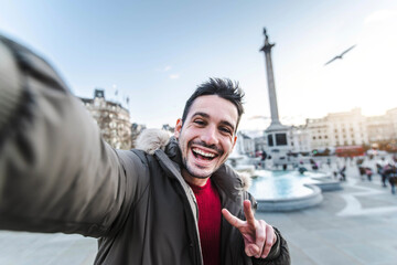 Smiling man taking selfie portrait during travel in London, England - Young tourist male taking memory pic with iconic england landmark - Happy people wandering around Europe concept - obrazy, fototapety, plakaty