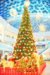 A defocused image of a tall, dressed up Christmas tree in the lobby of a shopping mall. Pre-holiday atmosphere. Blurred background picture