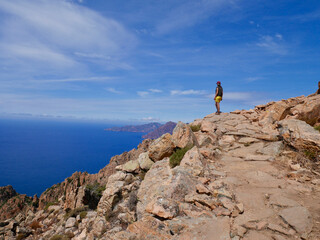 Woman looking at the red cliffs of the Calanche, UNESCO world heritage, and the Golf of Porto. Corsica, France.