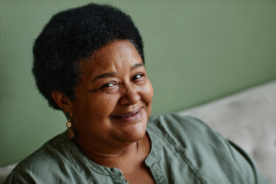Portrait of black senior woman smiling at camera against green background at home, copy space