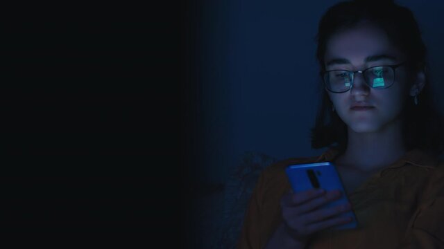 alone teen girl sits in the evening near tv and uses the phone, read some information
