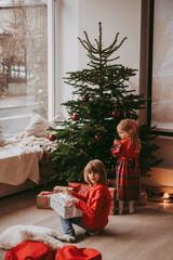 Obraz na płótnie Canvas Cute happy excited children, boy and girl unwrap christmas presents on holiday morning in beautiful room. Dressing decorating christmas tree. Sister and brother open Xmas gifts near decorated tree. 