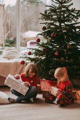 Cute happy excited children, boy and girl unwrap christmas presents on holiday morning in beautiful room. Dressing decorating christmas tree. Sister and brother open Xmas gifts near decorated tree. 