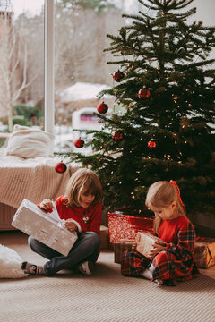 Cute happy excited children, boy and girl unwrap christmas presents on holiday morning in beautiful room. Dressing decorating christmas tree. Sister and brother open Xmas gifts near decorated tree. 