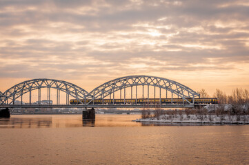 Electric train on the steel railway bridge at sunrise spring morning. Riga, Latvia.