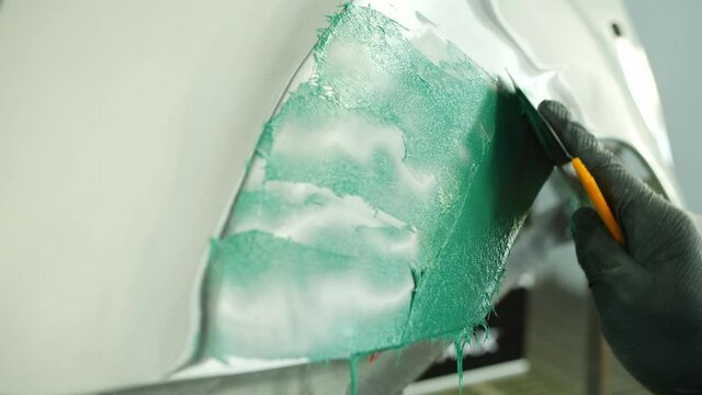 Covering a car part with green filler or coating with putty knife in repair shop
