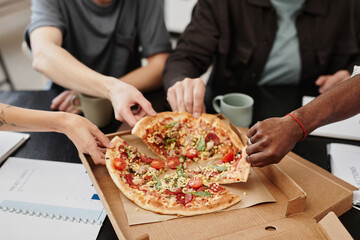Close-up of business people taking pieces of pizza during lunch while sitting at the table at office